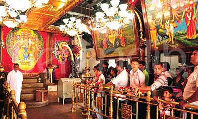 Inside the Maha Devale, the inner sanctum covered by a red curtain with a portrait of God Skanda on his peacock mount flanked by his two consorts, the crowd of devotees waits in anticipation for the puja to begin.